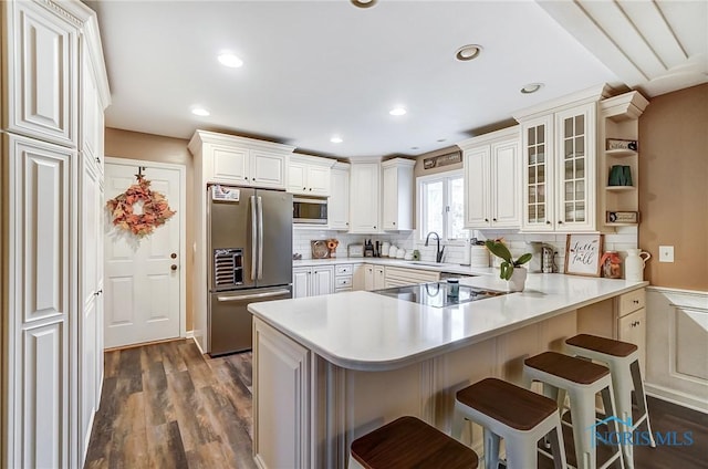 kitchen with glass insert cabinets, stainless steel appliances, dark wood-style floors, a kitchen bar, and a peninsula