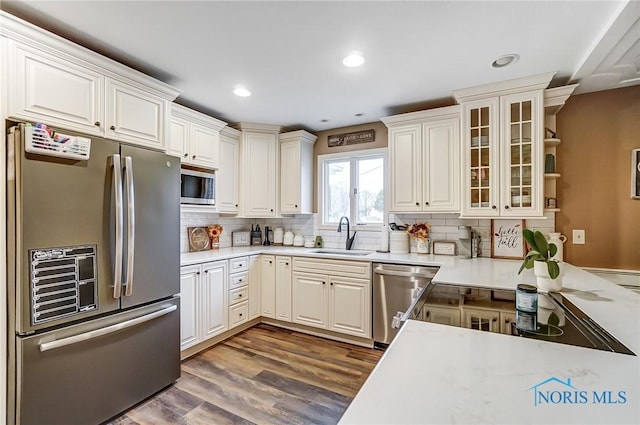 kitchen featuring a sink, stainless steel appliances, tasteful backsplash, dark wood-type flooring, and light countertops