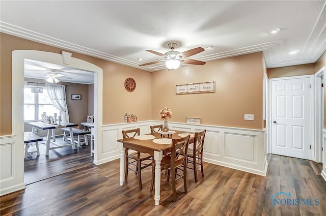 dining space with dark wood-type flooring, ceiling fan, a decorative wall, and a wainscoted wall