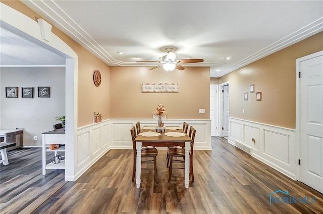 dining room with dark wood-style floors, wainscoting, ornamental molding, and ceiling fan