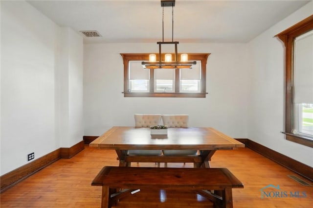 dining space featuring light wood-type flooring, visible vents, baseboards, and an inviting chandelier