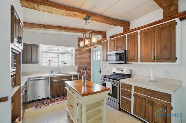 kitchen featuring stainless steel appliances, a sink, beamed ceiling, butcher block counters, and hanging light fixtures