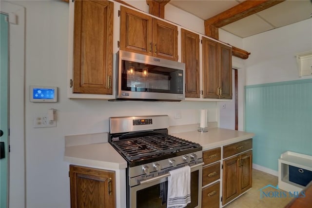 kitchen featuring brown cabinets, appliances with stainless steel finishes, a wainscoted wall, and light countertops
