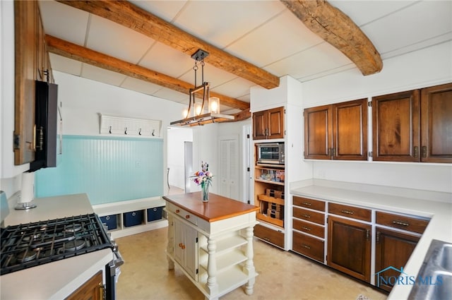 kitchen featuring beamed ceiling, light countertops, stainless steel microwave, and gas range