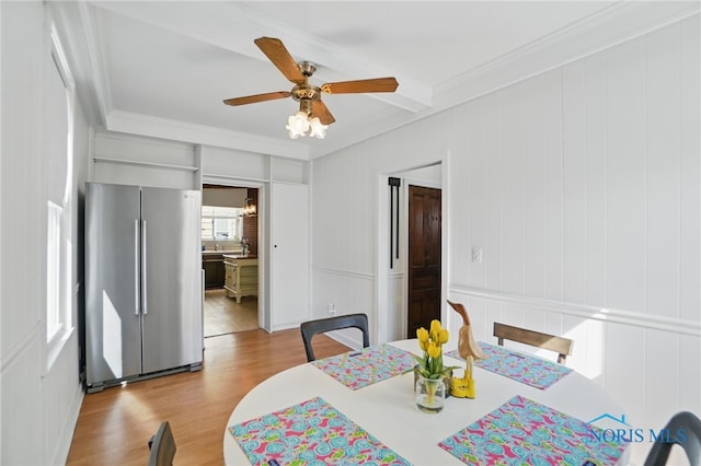 dining area with a decorative wall, wood finished floors, ceiling fan, beamed ceiling, and ornamental molding