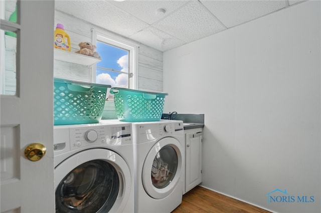 clothes washing area with wood finished floors, a sink, washer and clothes dryer, and cabinet space