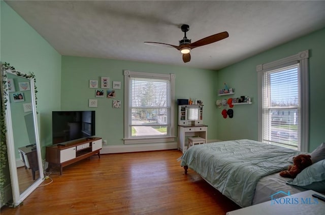 bedroom with baseboards, a ceiling fan, wood finished floors, and multiple windows