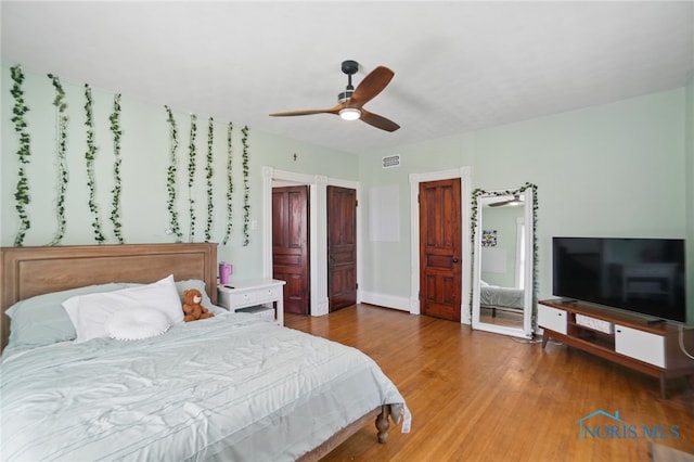 bedroom with wood finished floors, visible vents, baseboards, and ceiling fan