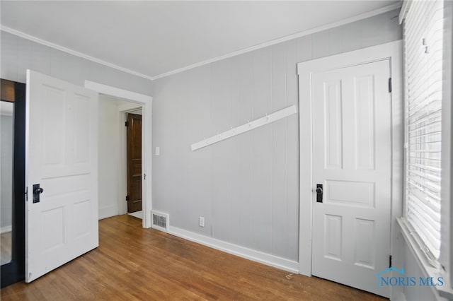 spare room with wood finished floors, visible vents, baseboards, and ornamental molding