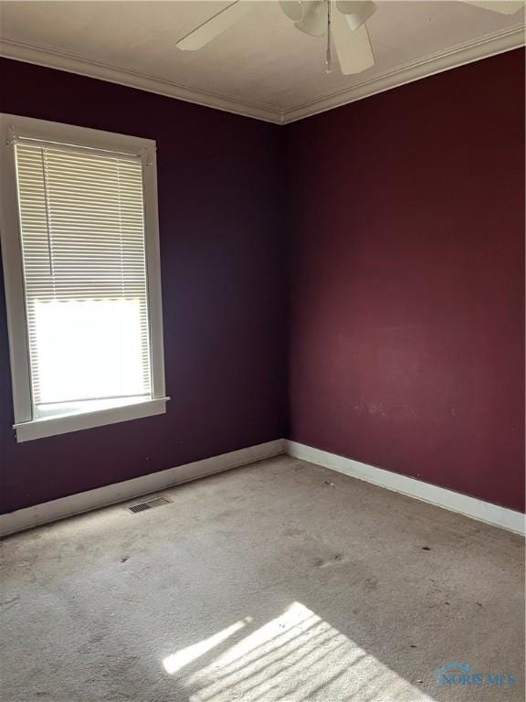 empty room featuring baseboards, visible vents, carpet, a ceiling fan, and crown molding