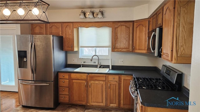 kitchen featuring brown cabinets, appliances with stainless steel finishes, a sink, and dark countertops