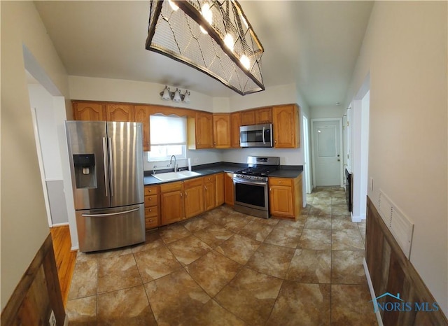 kitchen with brown cabinetry, dark countertops, appliances with stainless steel finishes, and a sink