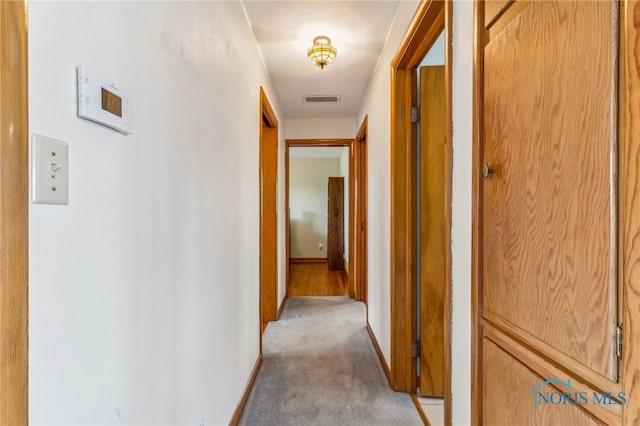 hallway with light colored carpet, baseboards, and visible vents