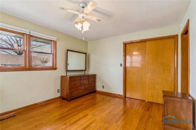 unfurnished bedroom featuring light wood-type flooring, baseboards, visible vents, a ceiling fan, and a closet