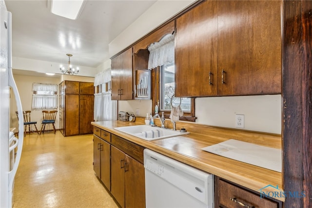 kitchen with brown cabinets, light countertops, a sink, white dishwasher, and a chandelier