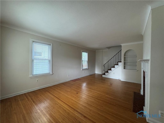 3721 Kershaw Ave, Toledo, OH 43613 - unfurnished living room featuring wood finished floors, stairs, a brick fireplace, a textured ceiling, and baseboards