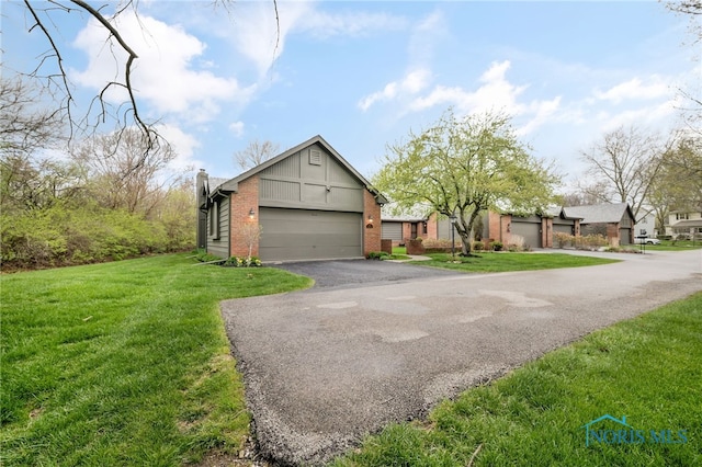 view of front of house featuring a chimney, brick siding, a garage, driveway, and a front yard