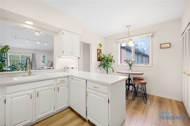 kitchen featuring a peninsula, dishwasher, light wood-style flooring, and a sink