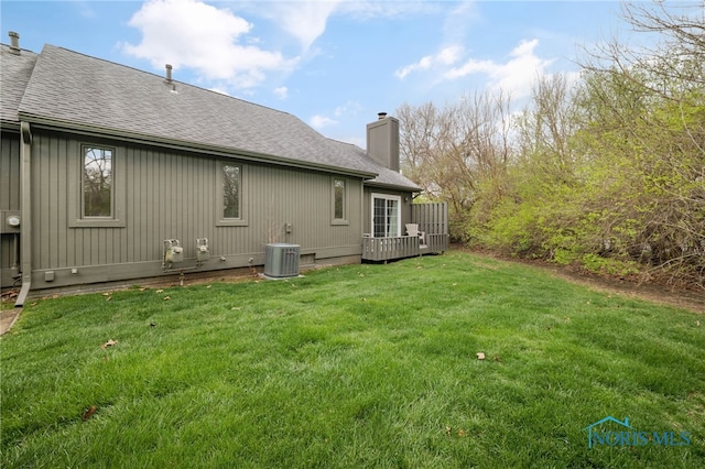 rear view of property featuring a wooden deck, a lawn, a shingled roof, and a chimney