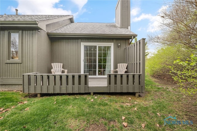 back of house featuring a wooden deck, a shingled roof, a chimney, and a yard