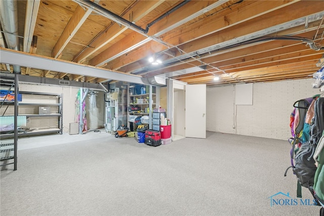 unfinished basement with visible vents, carpet floors, and brick wall