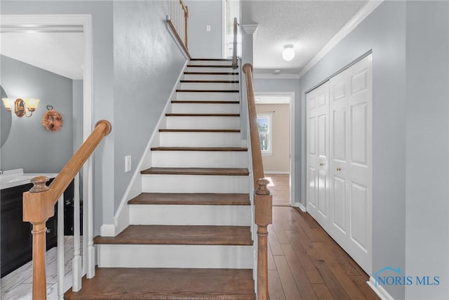 stairway with wood-type flooring, crown molding, a textured ceiling, and baseboards