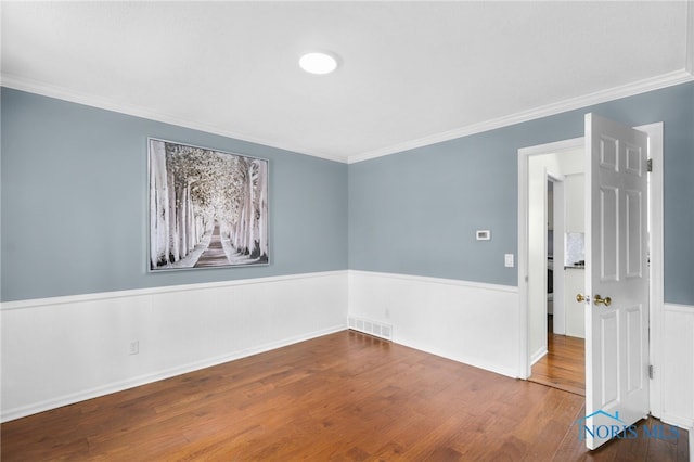 unfurnished room featuring crown molding, visible vents, wainscoting, and wood finished floors