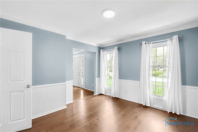 empty room featuring wainscoting, wood finished floors, and crown molding
