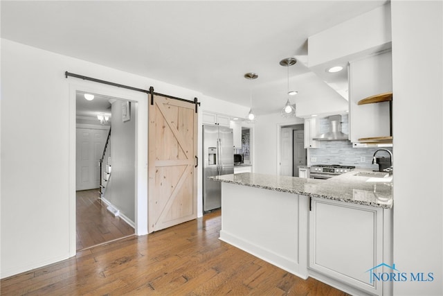 kitchen with open shelves, appliances with stainless steel finishes, a barn door, wall chimney exhaust hood, and a peninsula