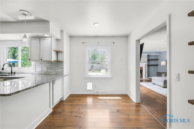 kitchen with decorative backsplash, visible vents, stone countertops, hardwood / wood-style floors, and decorative light fixtures