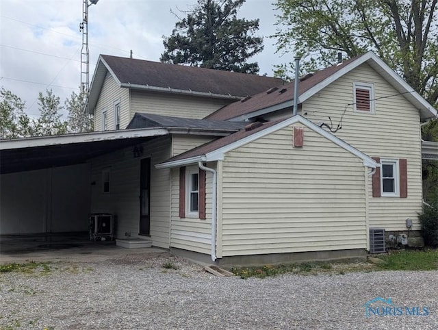 view of side of property with central air condition unit, gravel driveway, and an attached carport
