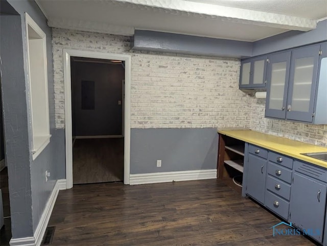 kitchen featuring light countertops, baseboards, glass insert cabinets, and dark wood-type flooring