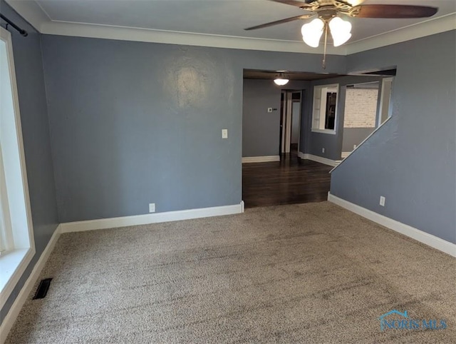 carpeted empty room featuring a ceiling fan, baseboards, visible vents, and ornamental molding