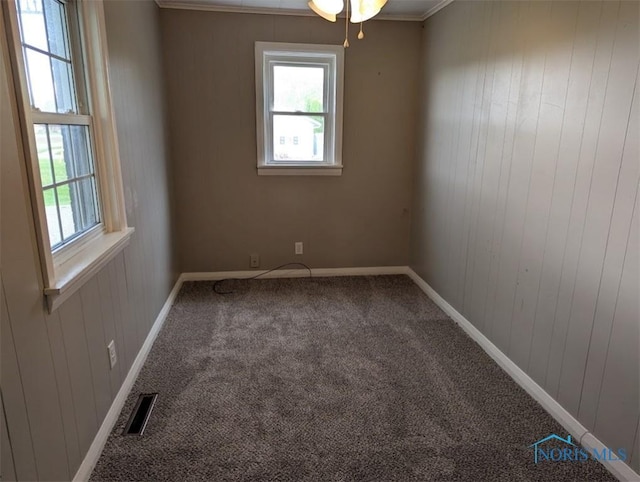 carpeted empty room with visible vents, ornamental molding, baseboards, and plenty of natural light