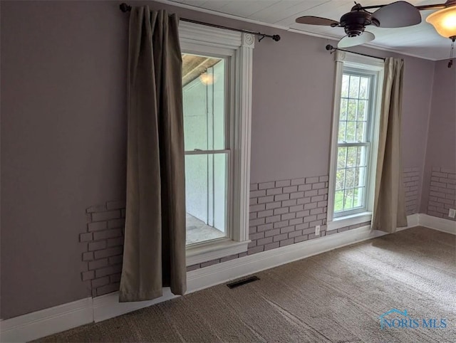 carpeted empty room with baseboards, plenty of natural light, a ceiling fan, and visible vents