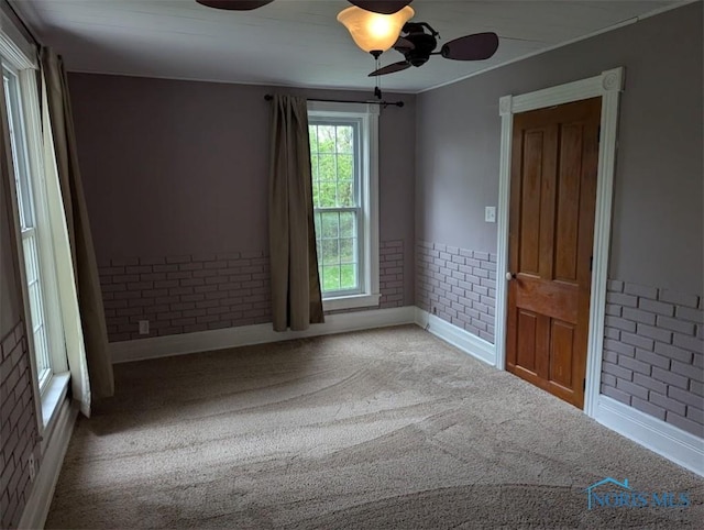 carpeted spare room with baseboards, a ceiling fan, and brick wall