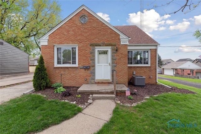 5583 304th St, Toledo, OH 43611 - bungalow-style house with central air condition unit, a shingled roof, brick siding, and a front lawn