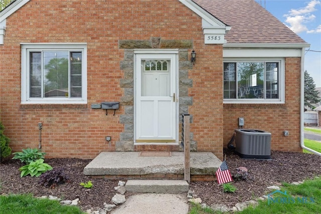 5583 304th St, Toledo, OH 43611 - view of exterior entry with a shingled roof, brick siding, and central AC