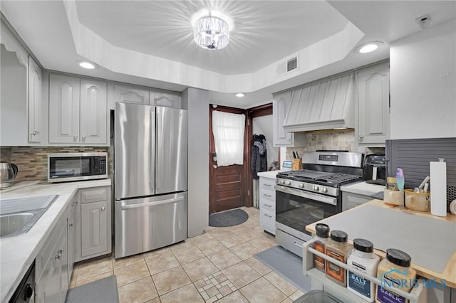 2923 Powhattan Pkwy, Toledo, OH 43606 - kitchen with appliances with stainless steel finishes, light tile patterned floors, a raised ceiling, custom exhaust hood, and light countertops
