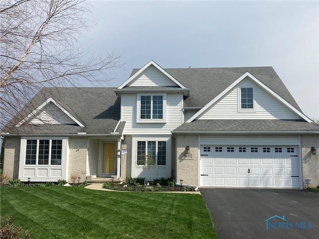 traditional home featuring a front yard, a shingled roof, a garage, brick siding, and aphalt driveway
