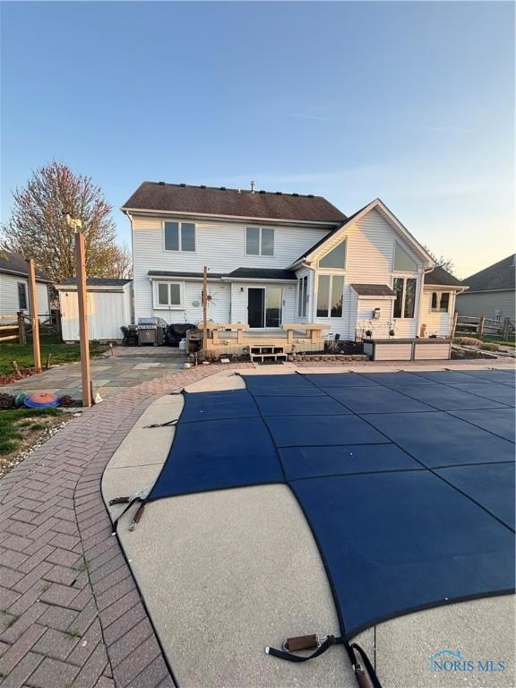 rear view of property featuring a covered pool and a patio area