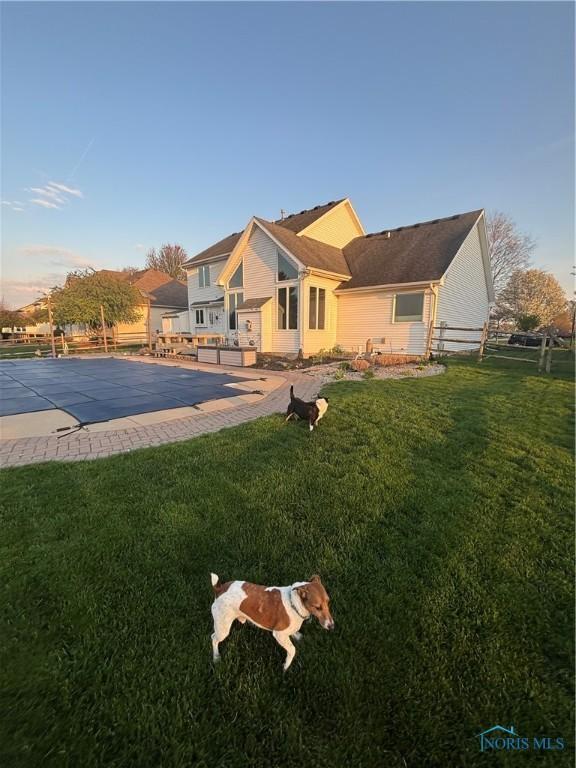 back of property with fence, a covered pool, and a lawn