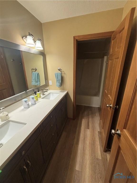 bathroom with wood finished floors, a textured ceiling, double vanity, and a sink