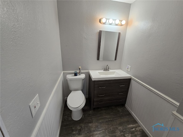 half bathroom featuring toilet, vanity, a textured wall, and wood finished floors