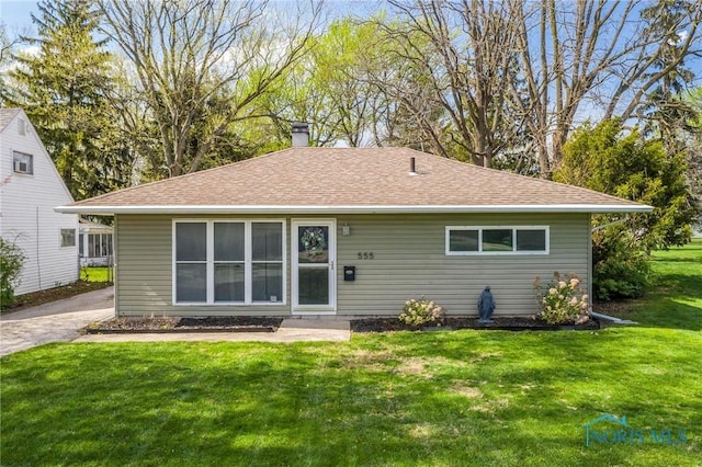 back of property with roof with shingles, a yard, and a chimney