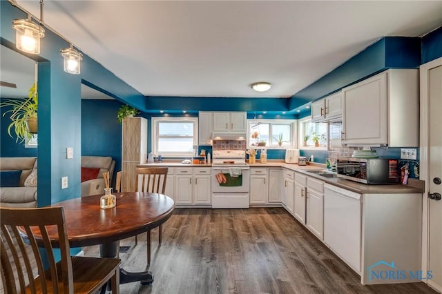 kitchen with white appliances, under cabinet range hood, white cabinets, a sink, and dark wood-style floors