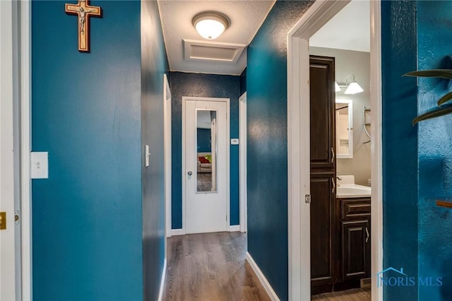 hall featuring attic access, a sink, wood finished floors, and baseboards