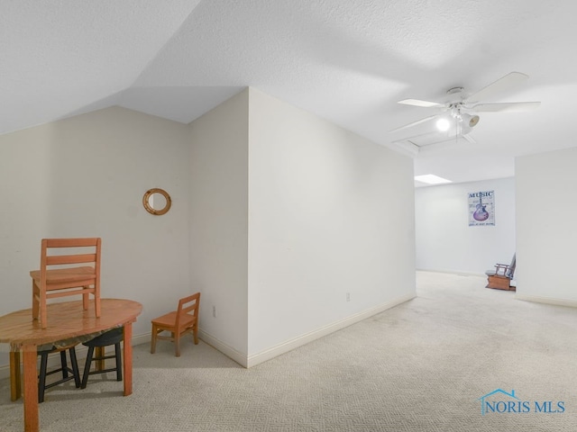 interior space with a ceiling fan, carpet, baseboards, a textured ceiling, and lofted ceiling