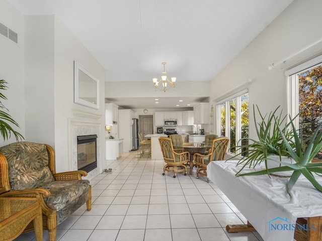 living room featuring light tile patterned floors, visible vents, a tiled fireplace, and a notable chandelier