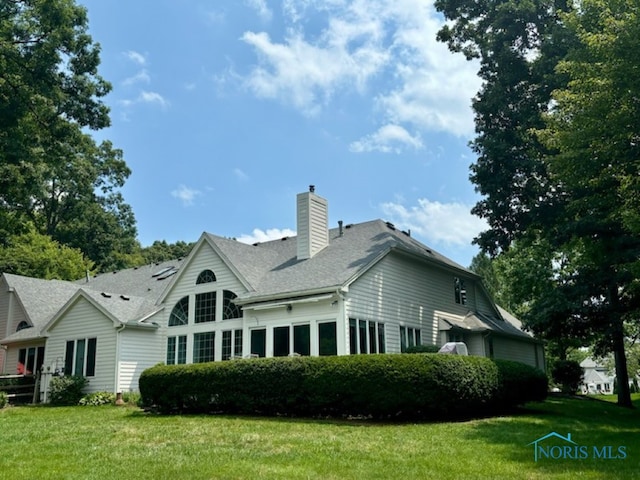 rear view of property with roof with shingles, a chimney, and a yard